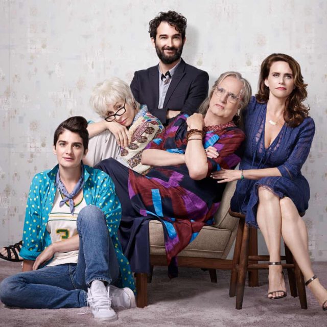 The main cast of the TV show TRANSPARENT posed in a family portrait, i.e., trans male-to-female father Maura, son Joshua, Mom Shelly, Daughters Sarah and Alexandra. They are dressed in hip outfits and have happy expressions.